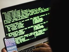 unrecognizable hacker with smartphone typing on laptop at desk
