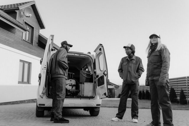 grayscale photo of people wearing coveralls standing beside a service van