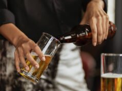 a person pouring beer on a clear drinking glass